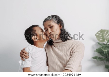 kiss the cheek, Asian grandson and grandmother people sitting together at desk.