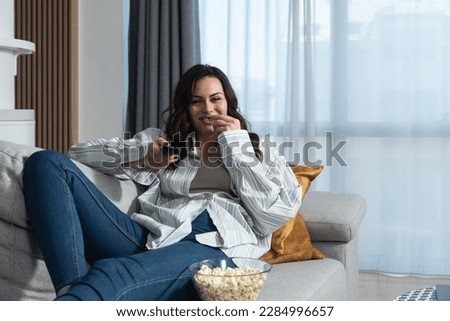 Young business woman day off relaxing on the couch, using remote control and choosing a TV show or movie on the television menu. Free female spending alone day at home, weekend activity concept