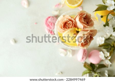 Glass of cocktail, ingredients and flowers on white textured table