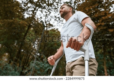 Walking, view from below. Man with crutches is in the park outdoors. Having leg injury. Royalty-Free Stock Photo #2284999875