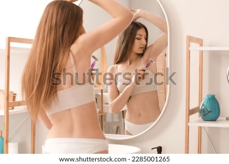 Pretty young woman shaving armpits in bathroom Royalty-Free Stock Photo #2285001265