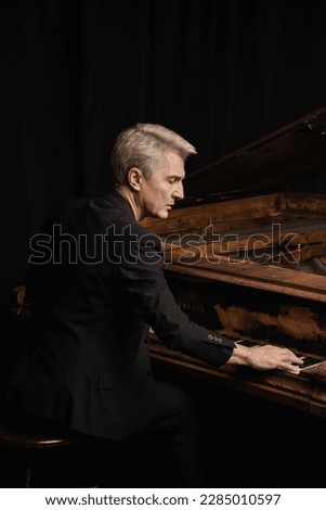 A male pianist in a suit on stage is a professional playing the piano on a black background.