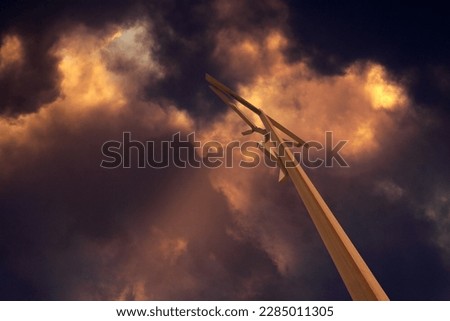 Wood cross against colorful stormy sky with heavy clouds and light beams at sunset