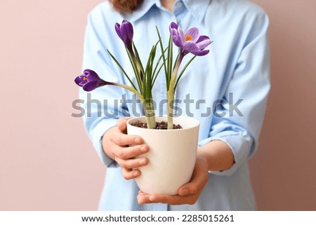 Woman holding pot with beautiful crocus flowers on beige background Royalty-Free Stock Photo #2285015261