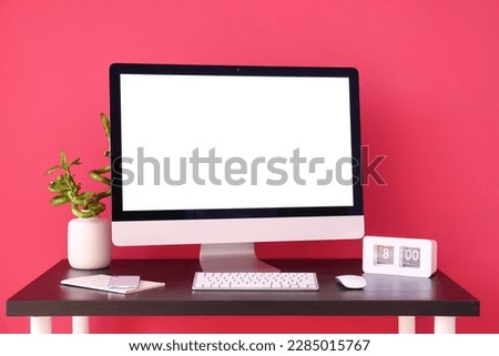 Workplace with computer, mobile phone and clock near red wall