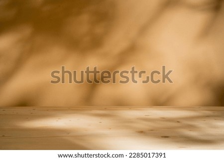 Mock up for presentation, branding products, cosmetics, food or jewellery. Empty table on bright brown wall background. Composition with leaves and trees shadows on the wall and wooden desk.  Royalty-Free Stock Photo #2285017391