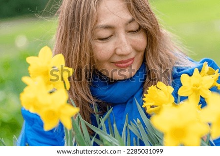 Asian woman in blue coat walking in a park among flowers on spring day