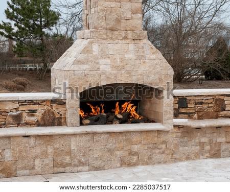A gas fireplace made from paving stone burning outside on a patio close up.
