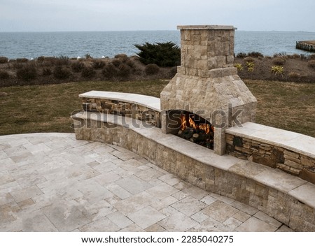 Stone fireplace burning on a patio of paving stone by the bay in a residential backyard.