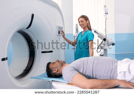 Medical equipment. Doctor and patient in the room of computed tomography at hospital. Young female doctor examining man in 40s with CT scanner. Computerised tomography.