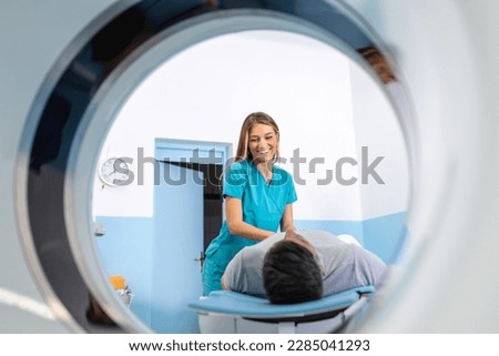 Doctor preparing patient for CT scanner. Senior man going into CT scanner. CT scan technologist overlooking patient in Computed Tomography scanner during preparation for procedure