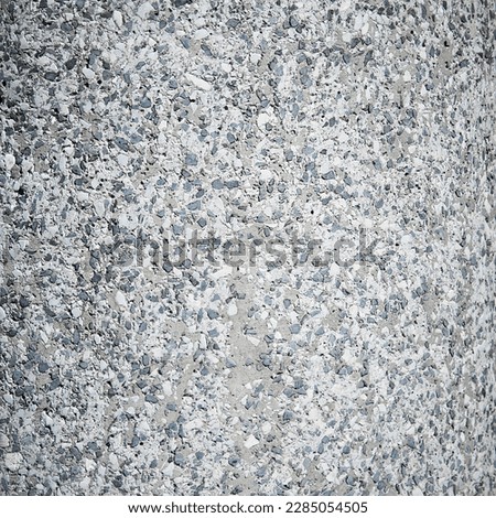 A texture of small stones in a gray-blue tone, the old rough wall of a thick column in the street. Random pattern