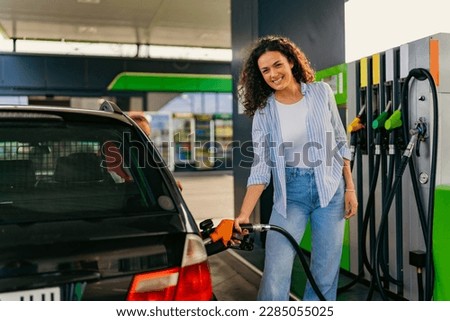 A young mother fills fuel while her daughters are waiting for her in the car Royalty-Free Stock Photo #2285055025