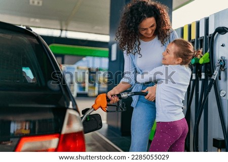 A mother pours fuel into the car while her daughter hugs her, both are happy Royalty-Free Stock Photo #2285055029