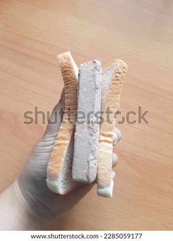 left hand holding a folded piece of white bread with chocolate ice cream inside on a wood-patterned table background