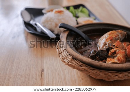 A picture of Ikan Kembung "asam pedas" with white rice on a wooden background. "Asam pedas" is sour soup made from tamarind, chilli and spices that is popular in Malaysia