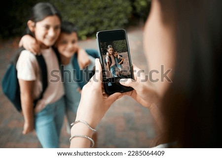 Children first day of school and mother taking photos with a phone of her cute kids. Closeup of screen picture of brother and sister embracing while posing for their mom outside in the morning