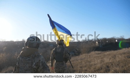 Female and male soldier of ukrainian army walking with flag of Ukraine at field. Woman and man in military uniform going with national banner at meadow as sign of victory against russian aggression. Royalty-Free Stock Photo #2285067473