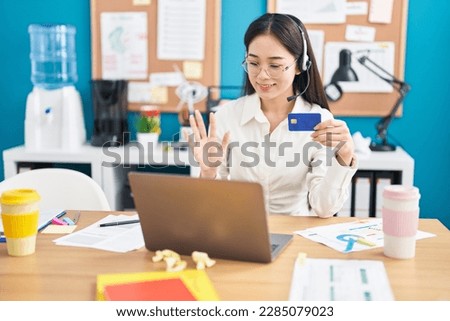 Young chinese woman working at the office doing online shopping looking positive and happy standing and smiling with a confident smile showing teeth 