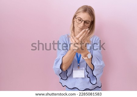 Young caucasian business woman wearing id card suffering pain on hands and fingers, arthritis inflammation 