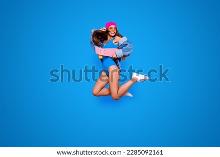 Full length size studio photo shooting portrait of cheerful joyful careless fresh cool with toothy beaming smile girl jumping up with skate board in hand isolated bright pastel background