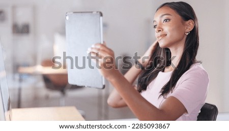 Young happy woman taking a selfie with a digital tablet while relaxing in an office at work. One smiling female student taking pictures to post on social media while sitting alone in a library