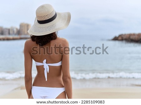 Young african american woman wearing summer hat and bikini standing on back view at beach
