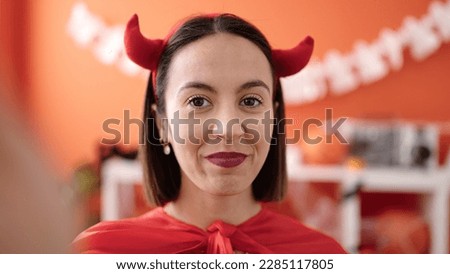 Young beautiful hispanic woman wearing devil costume make selfie by camera at home