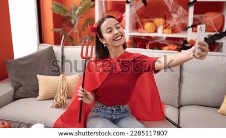 Young beautiful hispanic woman wearing devil costume make selfie by smartphone at home
