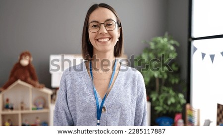 Young beautiful hispanic woman teacher smiling confident standing at kindergarten