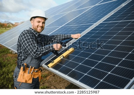 Portrait of smiling confident engineer technician with electrical screwdriver, standing in front of unfinished high exterior solar panel photo voltaic system. Royalty-Free Stock Photo #2285125987