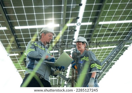 A team of electrical engineers is inspecting and maintaining solar panels at a solar panel site in the middle of a hundred acre field. Royalty-Free Stock Photo #2285127245