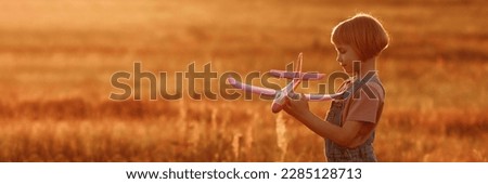 The girl runs across the summer field and launches a toy plane into the sky. A child plays aviator or pilot in a field at sunset, a happy childhood. Banner for website header design with copy space.