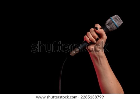 Hand of person holding microphone. Singer with his microphone in hand. Microphone on black background. Woman's hand holding up a microphone
