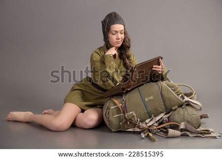 girl in uniform of the Soviet army and aviator cap sits on parachute and read