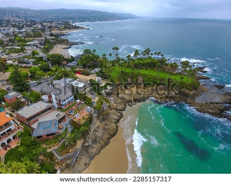 breathtaking aerial shot of the deep green ocean water, the beach, the rocks, the palm trees and homes on the beach on a cloudy day at Crescent Bay Beach in Laguna Beach California USA Royalty-Free Stock Photo #2285157317