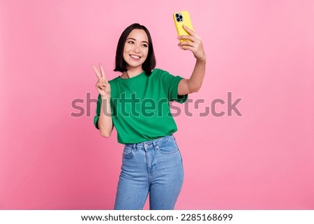 Photo of charming positive lady hold smart phone make selfie demonstrate v-sign isolated on pink color background