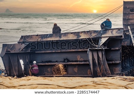 Shipbreaking of a large oil tanker in the harbor, labour cutting the parts through welding, with the background of sunset on the beach at Gadani Ship Breaking Yard, Pakistan Royalty-Free Stock Photo #2285174447