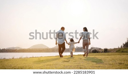 Happy family in the park sunset light. family on weekend running together in the meadow with river Parents hold the child hands.health life insurance plan concept. Royalty-Free Stock Photo #2285183901