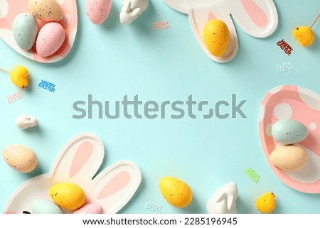 Easter frame border made of colorful Easter eggs, bunny and eggs shaped cutlery on pastel blue table.