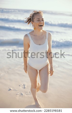 Full length portrait of happy stylish female in white swimwear at the beach walking.