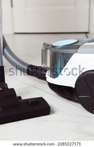 Vacuum cleaner with plastic dust container, hose and brush on flat ceramic floor tiles inside room, no people Royalty-Free Stock Photo #2285227171