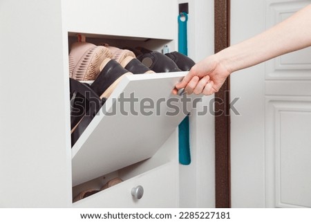 Woman opens Shoe Cabinet with Footwear in hallway. Storage ideas. Seasonal shoes storage. White interior Royalty-Free Stock Photo #2285227181