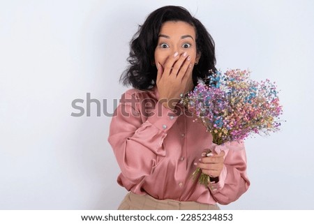 Vivacious beautiful woman wearing pink shirt over white background, giggles joyfully, covers mouth, has natural laughter, hears positive story or funny anecdote