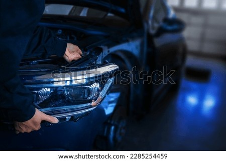 Skilled mechanic workInstalling new front headlight on a car with precision and expertise. Working in garage or auto service center. Detail shot of process with focus on a mechanic hands and tools. Royalty-Free Stock Photo #2285254459