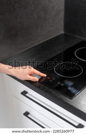 cropped shot of female hand press button on glass ceramic induction hob and select temperature mode on control panel, modern household appliances concept Royalty-Free Stock Photo #2285260977