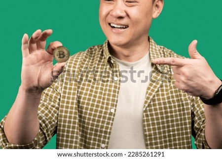 Digital cryptocurrency, trading on stocks and markets concept. Korean middle aged businessman holding golden bitcoin and pointing at it, cropped, closeup