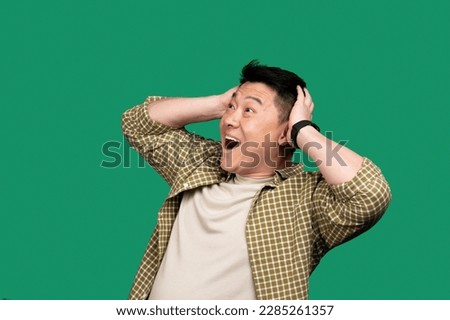 Shocked asian middle aged man opening mouth and touching head, surprised male standing over green studio background, emotionally reacting to news Royalty-Free Stock Photo #2285261357