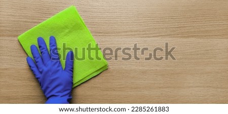 Banner with housewife hand and rag. Flat lay. Wiping Away. Place for text. Hand in rubber glove wipes down wooden table with help of dishcloth. Copy space. House cleaning concept. Top view.  Royalty-Free Stock Photo #2285261883