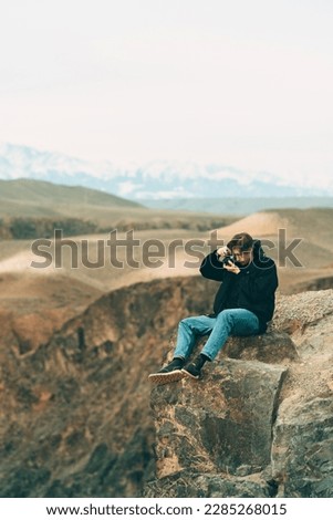 Photographer taking authentic outdoor photos on vintage camera in landscape sitting on a cliff High quality photo